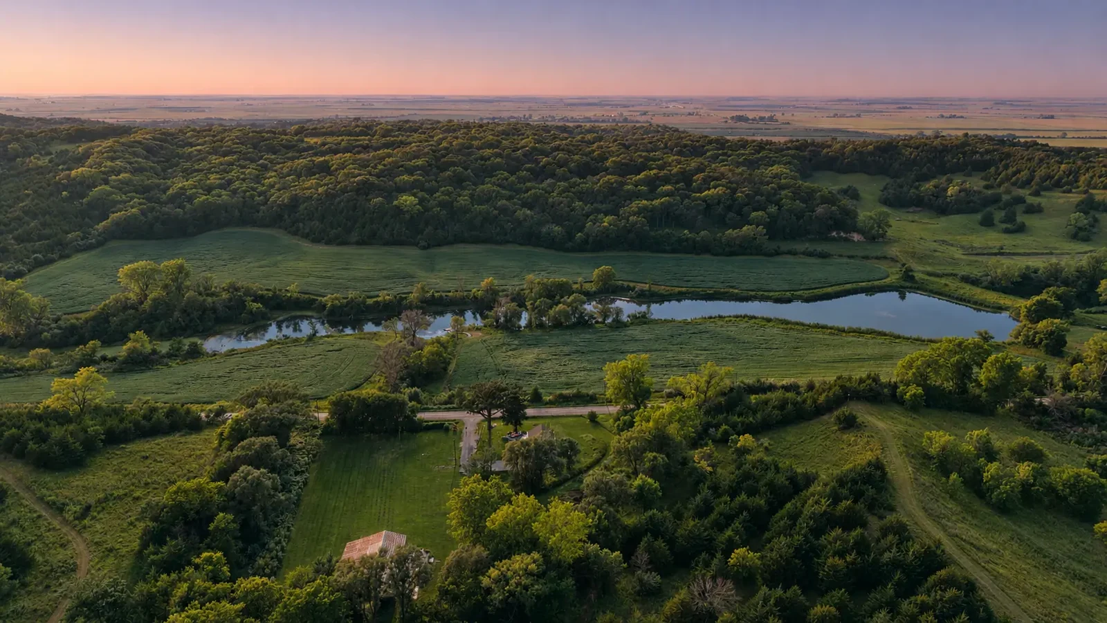 Wide aerial view of the private lakes, woodland and open fields beneath an Iowa sunset