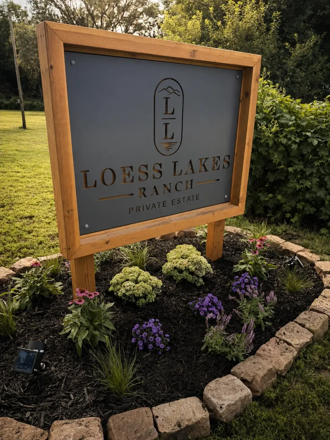 The LOESS LAKES RANCH PRIVATE ESTATE entrance sign in a cedar frame above a flower bed