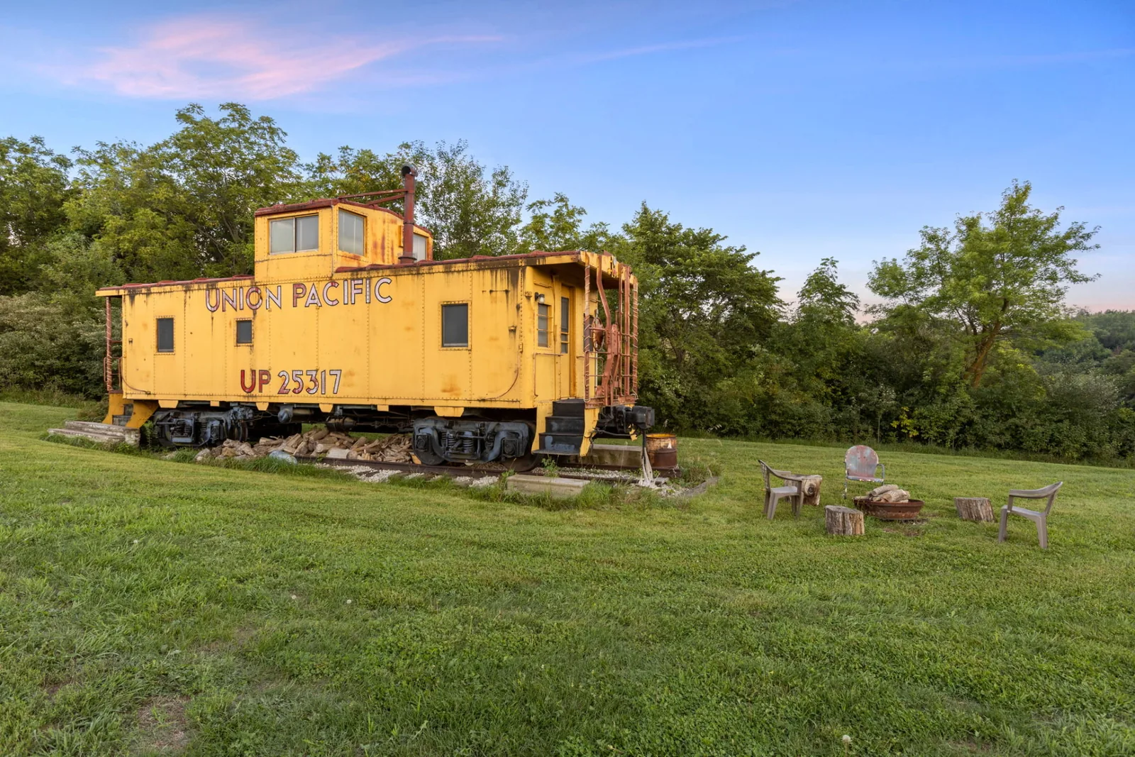 Vintage yellow Union Pacific caboose UP 25317 on a short section of track, with chairs around a fire ring on the mown lawn at dusk