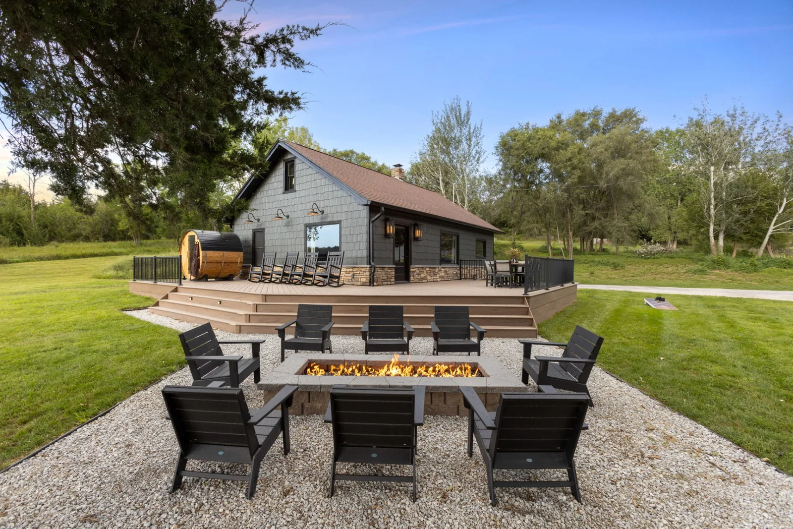 The ranch farmhouse, deck and cedar sauna behind a lit firepit surrounded by chairs
