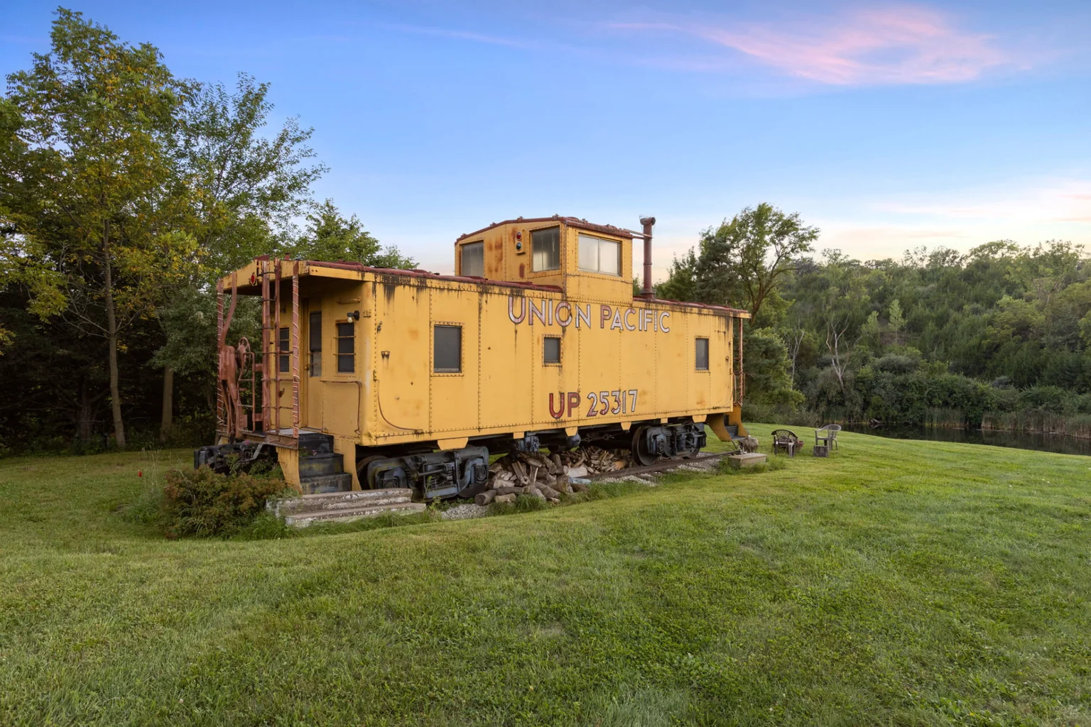 Vintage yellow Union Pacific caboose beside a ranch lake and wooded hills at sunset