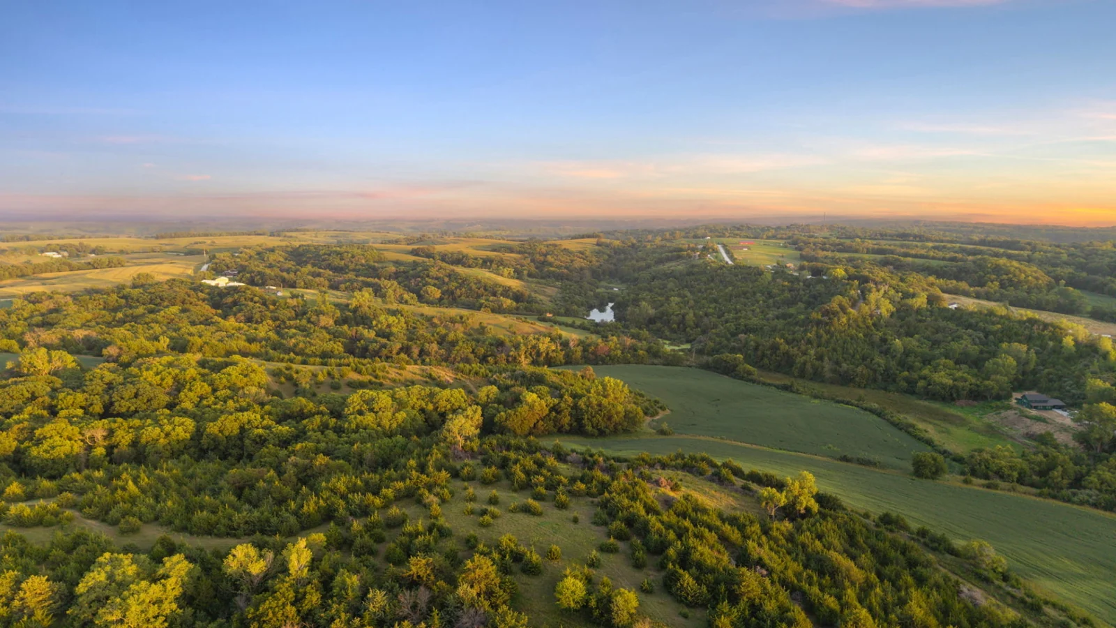 Aerial view of the rolling timber, open ground and valleys across Loess Lake Ranch at sunset.