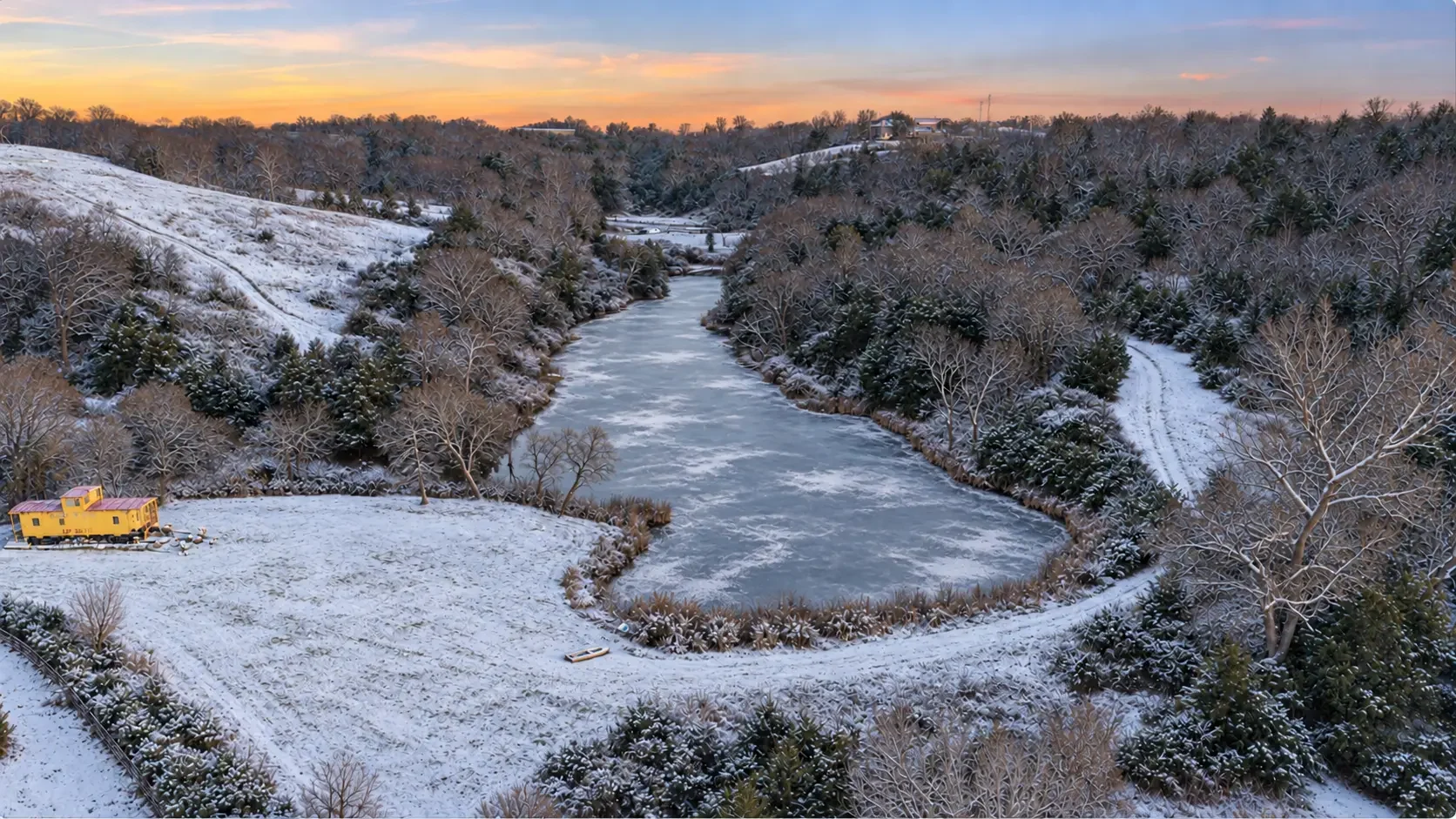 Aerial view of a frozen lake at Loess Lakes Ranch with the yellow caboose on the snowy shore at sunset