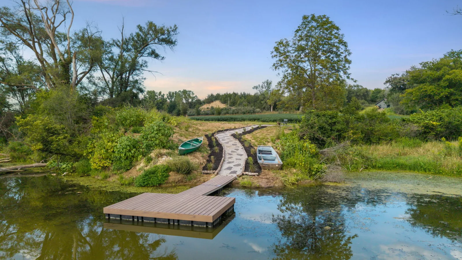 Wooden fishing dock on the private lake at dusk with a canoe and rowboat pulled up beside a stone path