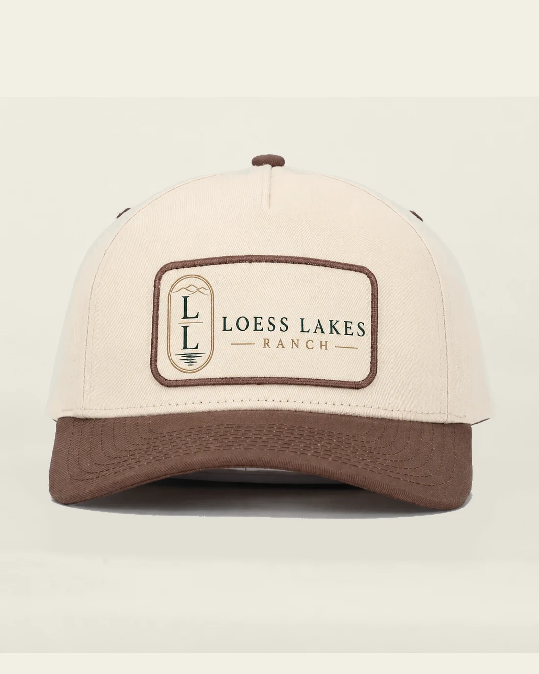 Front view of the cream Lodge Patch Cap with tobacco-brown bill and a stitched rectangular LOESS LAKES RANCH patch