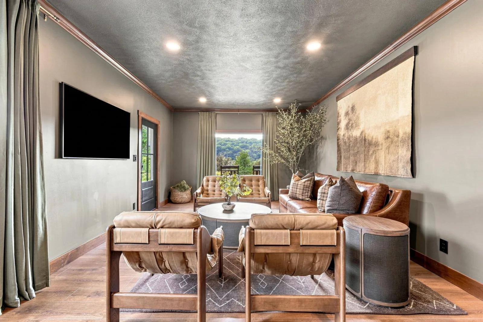 Living room at Loess Lakes Ranch with tan leather seating, a round coffee table, wall art and a window looking out to wooded hills