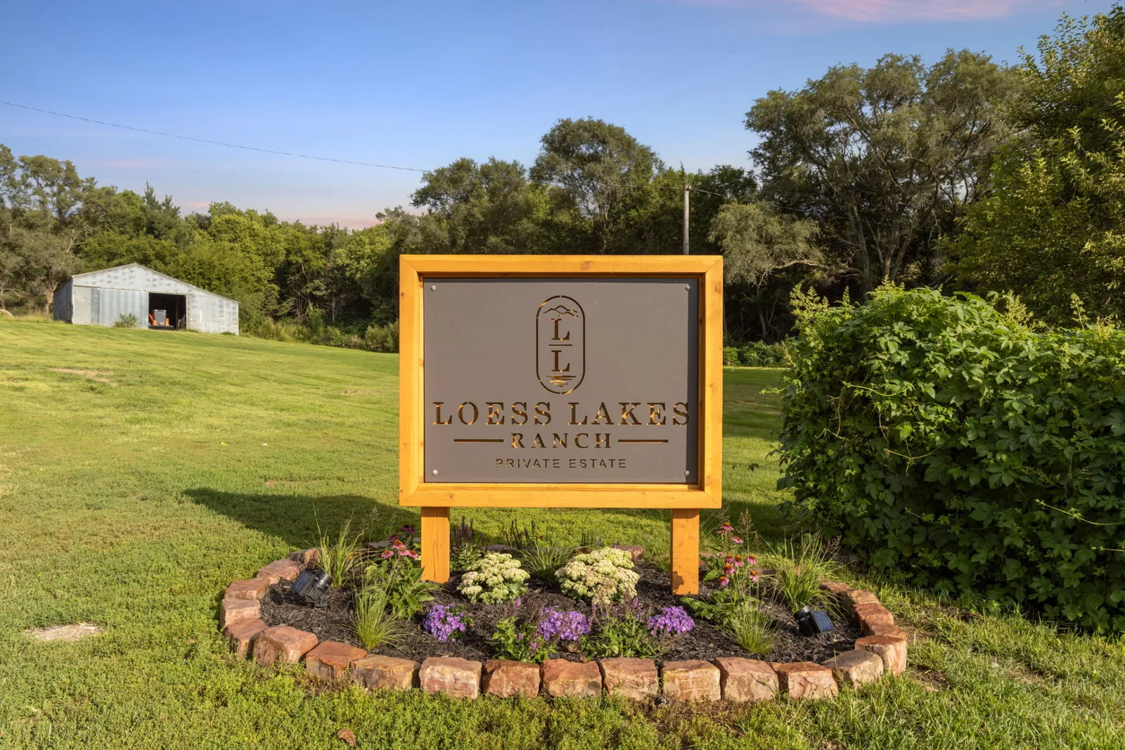 The LOESS LAKES RANCH PRIVATE ESTATE entrance sign in a cedar frame above a stone-edged flower bed