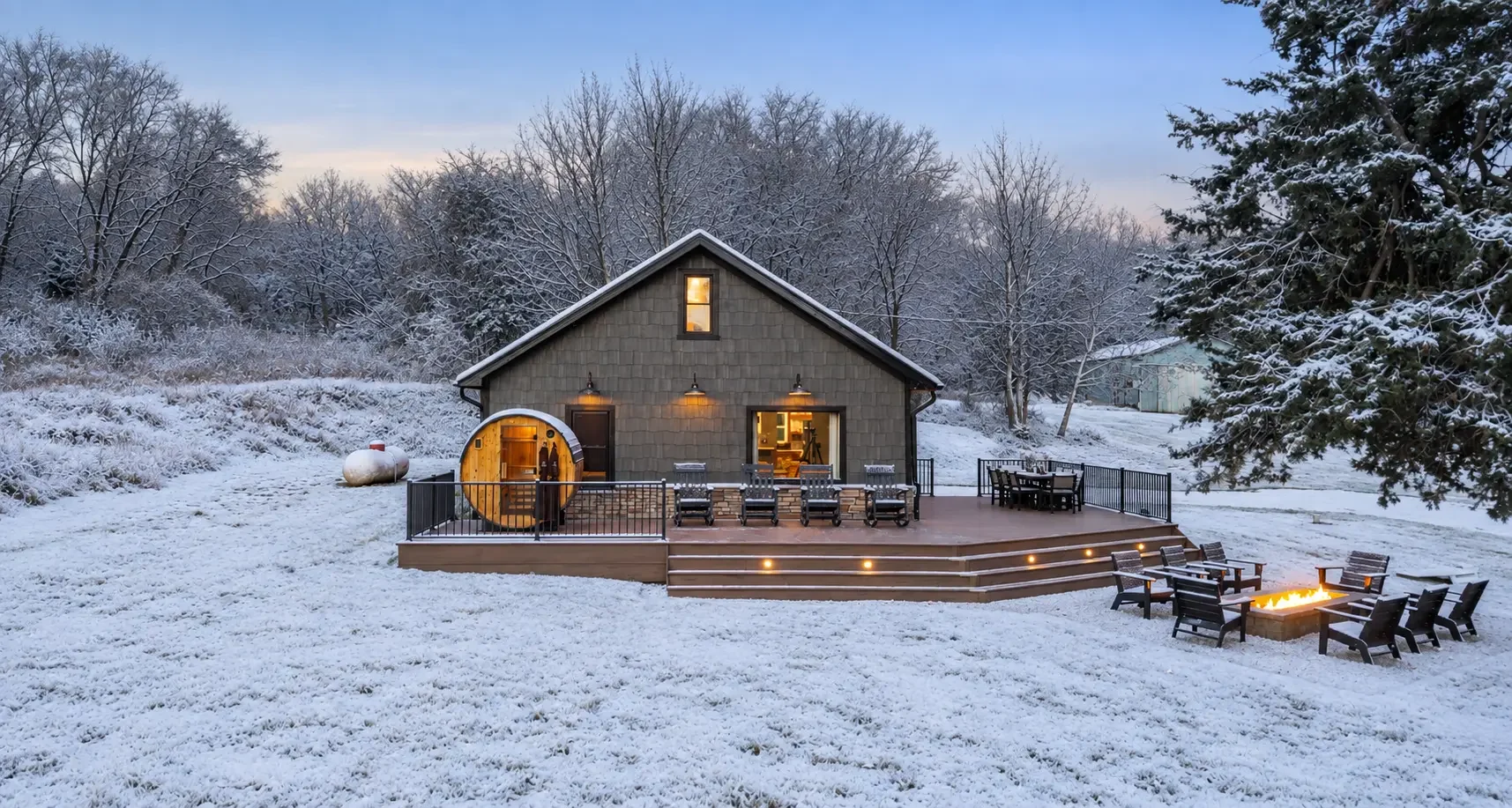 Loess Lakes Ranch lodge in winter with the barrel sauna, deck and glowing fire pit in fresh snow
