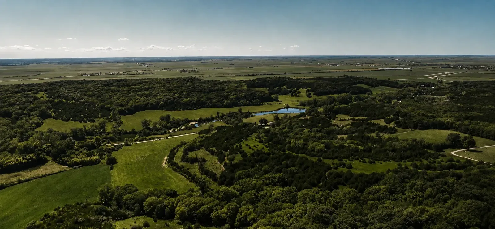 Daylight aerial view of the ranch: wooded hills, mown fields, the lake and the surrounding Loess Hills