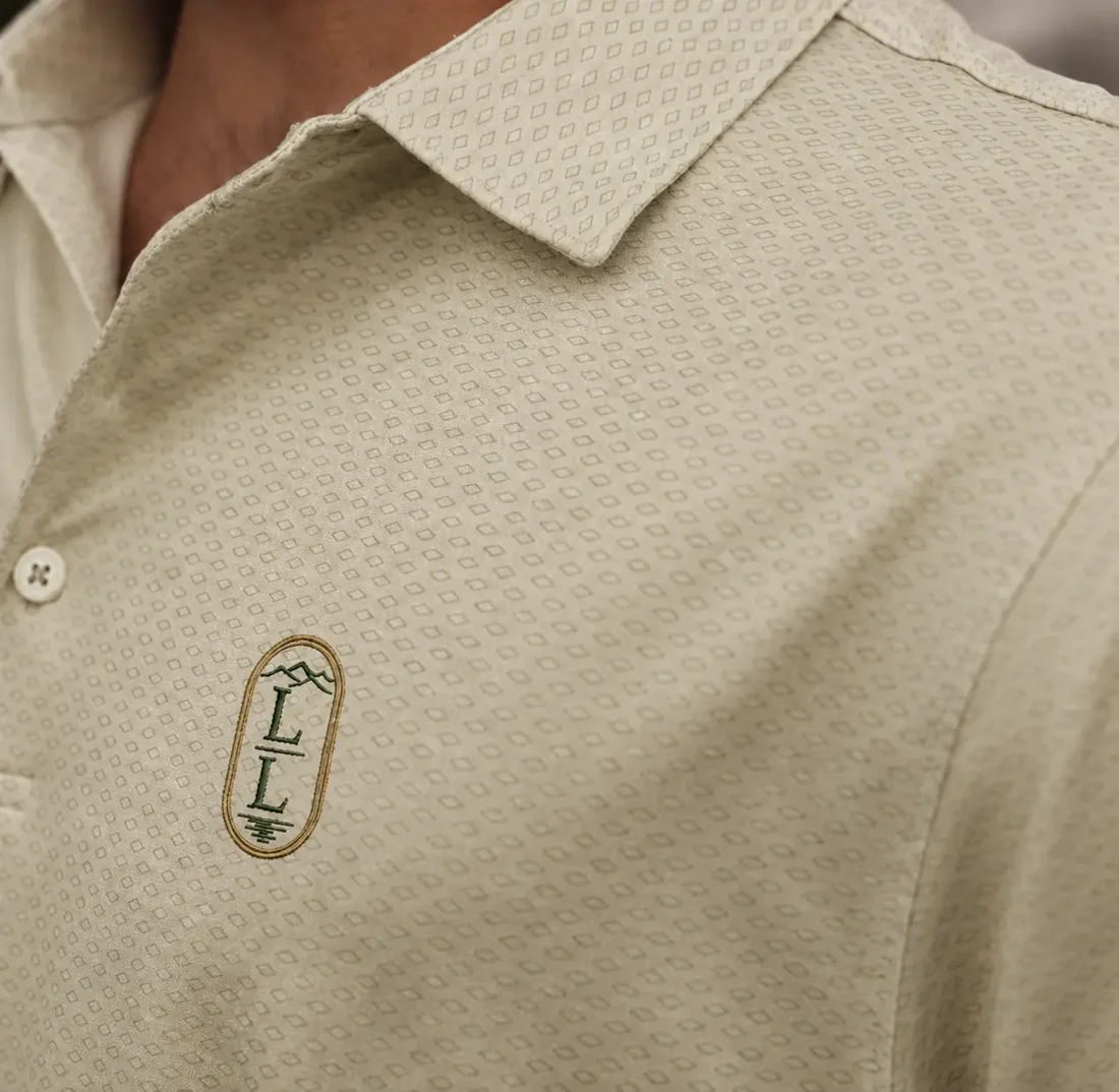 Close view of a cream patterned performance polo with an embroidered vertical LL crest in green and gold